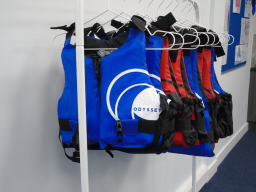 Row of brightly coloured life vests hanging on hooks in a storage area.