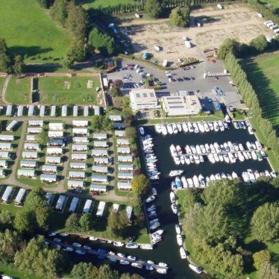 Aerial view of a marina with boats, caravans, and a surrounding green landscape.