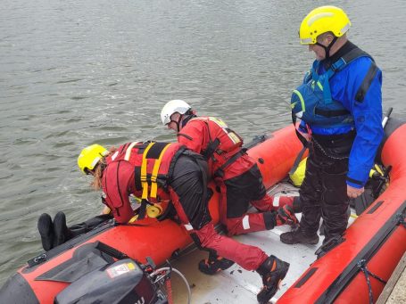 Two rescue workers assist a colleague on a rescue boat