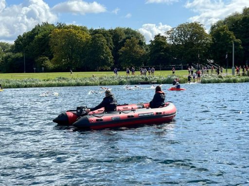 Two medical personnel in a boat as a swimming race goes on in the background