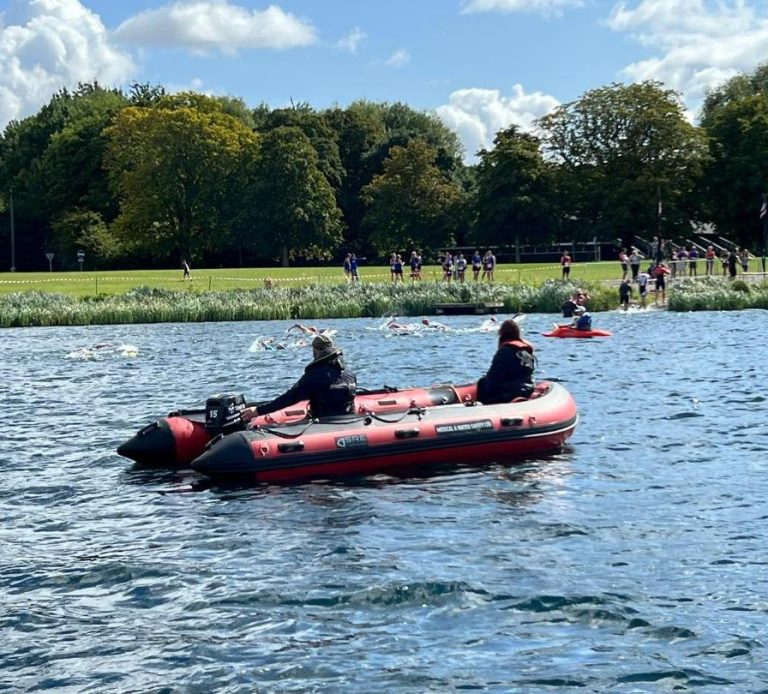Two medical personnel in a boat as a swimming race goes on in the background